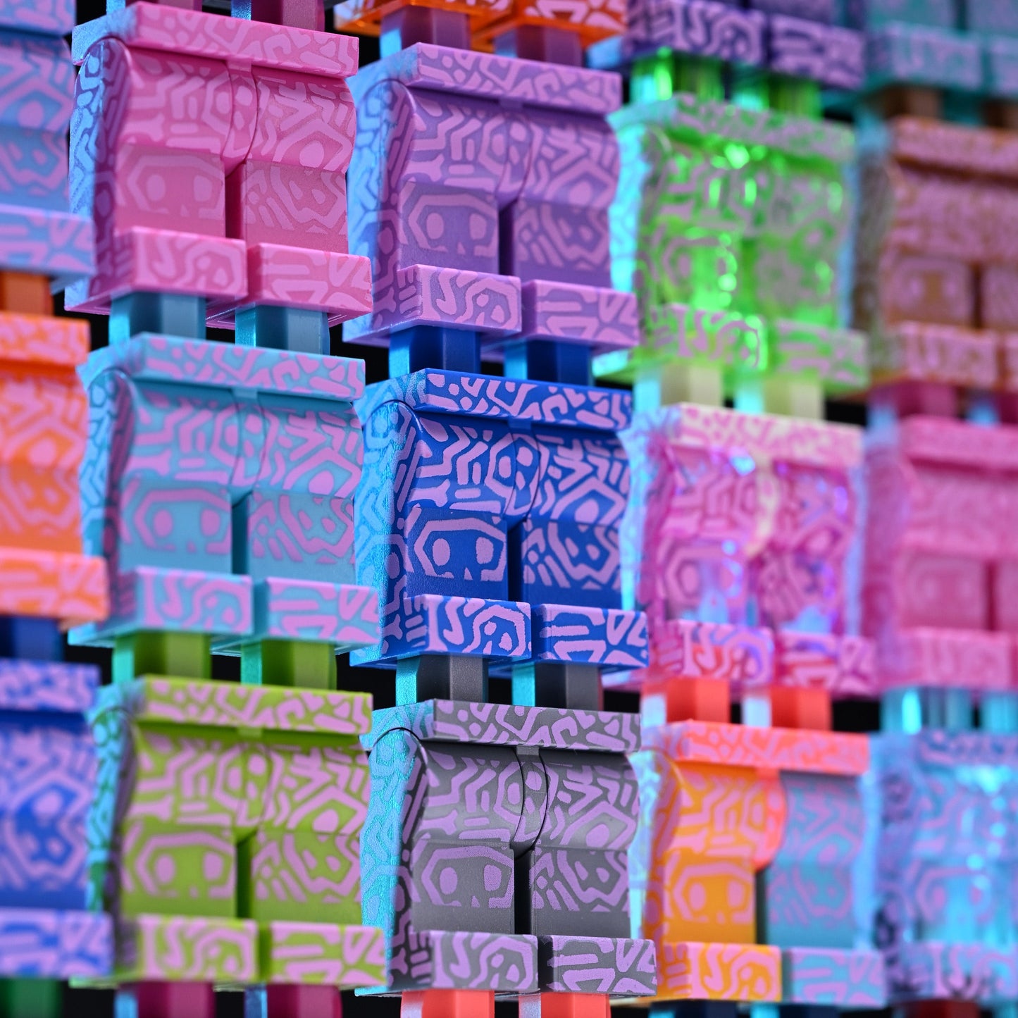 A close-up of a colorful, patterned skull design arranged in a grid. The items feature bright neon hues including pink, purple, blue, green, orange, and yellow, each with an intricate geometric maze-like pattern on their faces.